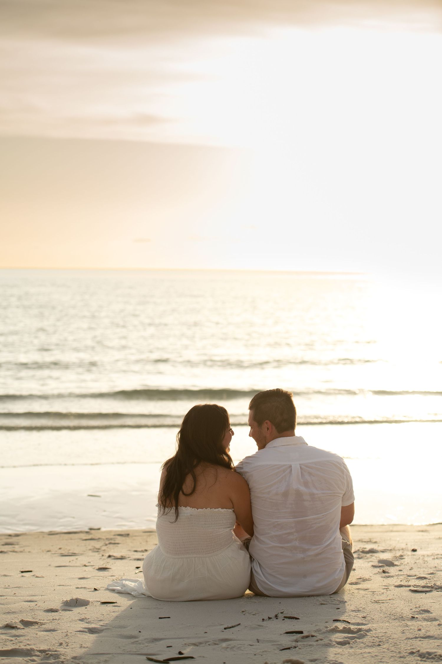 Couple sitting together on beach watching sunset over ocean horizon.
