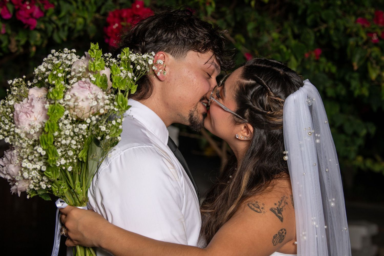 A tender moment between newlyweds with a floral bouquet against a backdrop of red flowering bushes. Wedding photography.