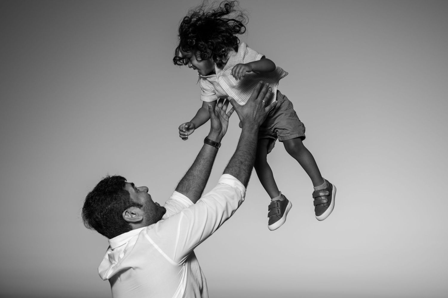 Black and white photos capture playful family moments against a plain background. Beach photoshoot. Family photoshoot,