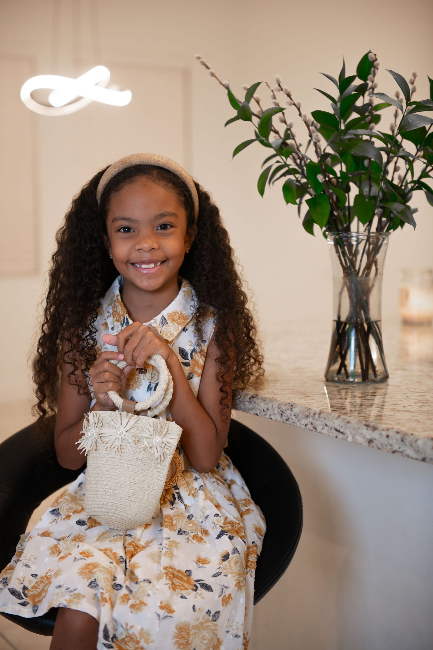 Young child in a floral dress sitting at a marble counter with indoor plants.