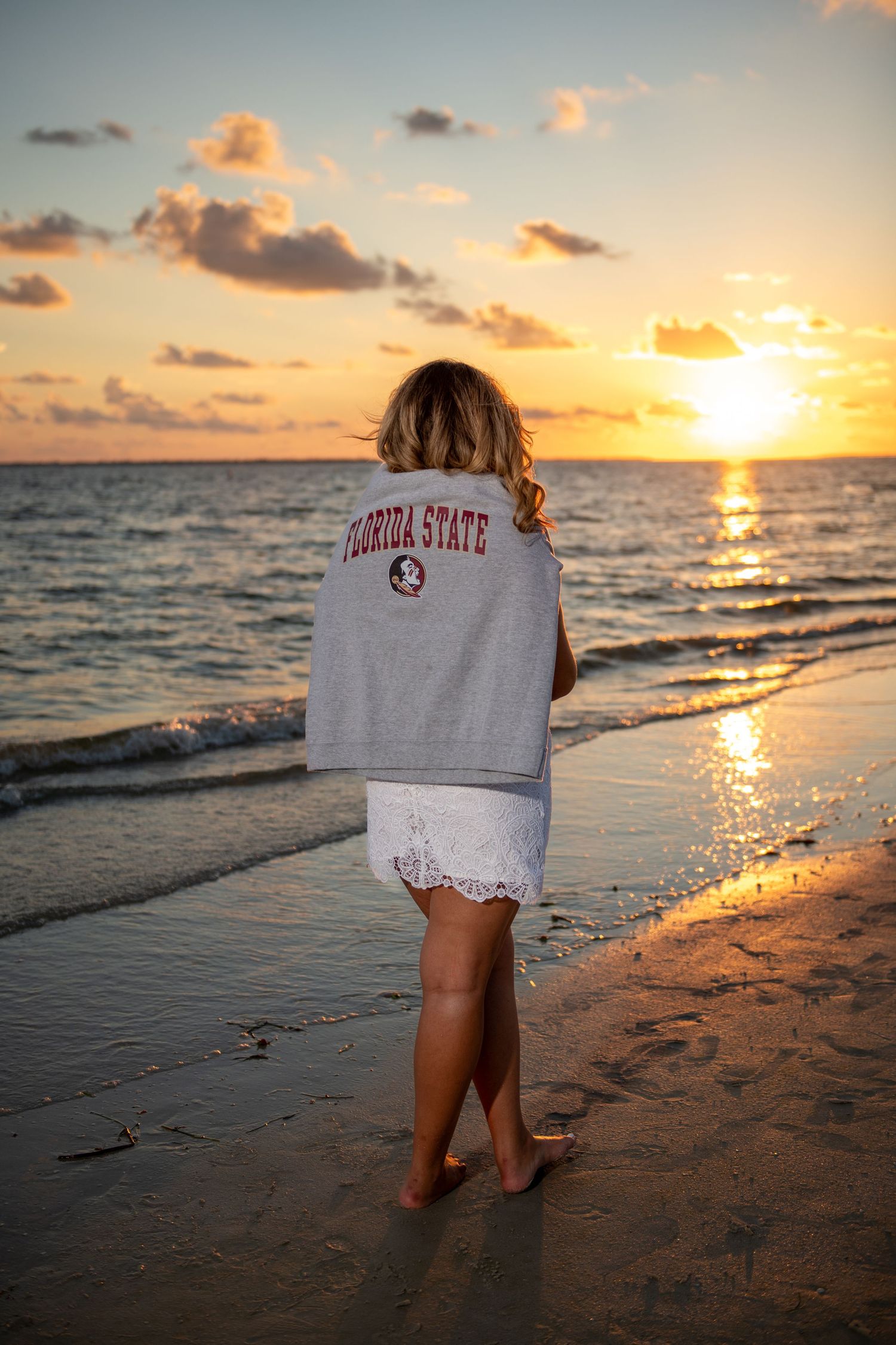 Person wearing Florida State sweatshirt watching sunset on beach.