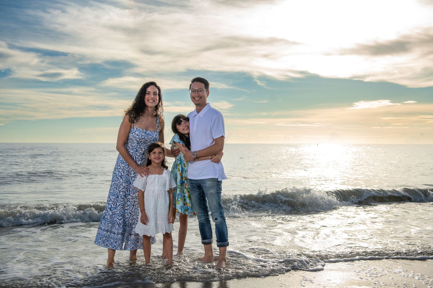 A family stands together on the beach at sunset with waves crashing behind them.