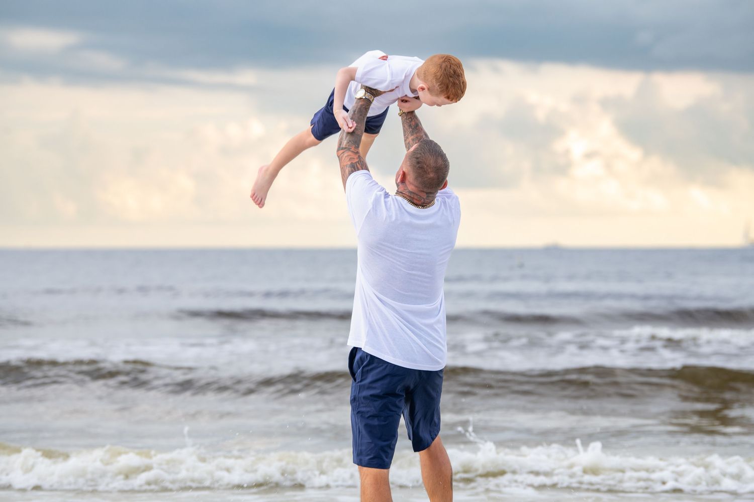 Family playing and splashing in ocean waves during golden hour photo session.