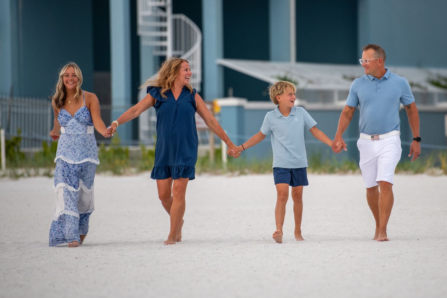 Family walking together on white sandy beach in coordinated blue and white outfits. Beach photoshoot. Family photoshoot,