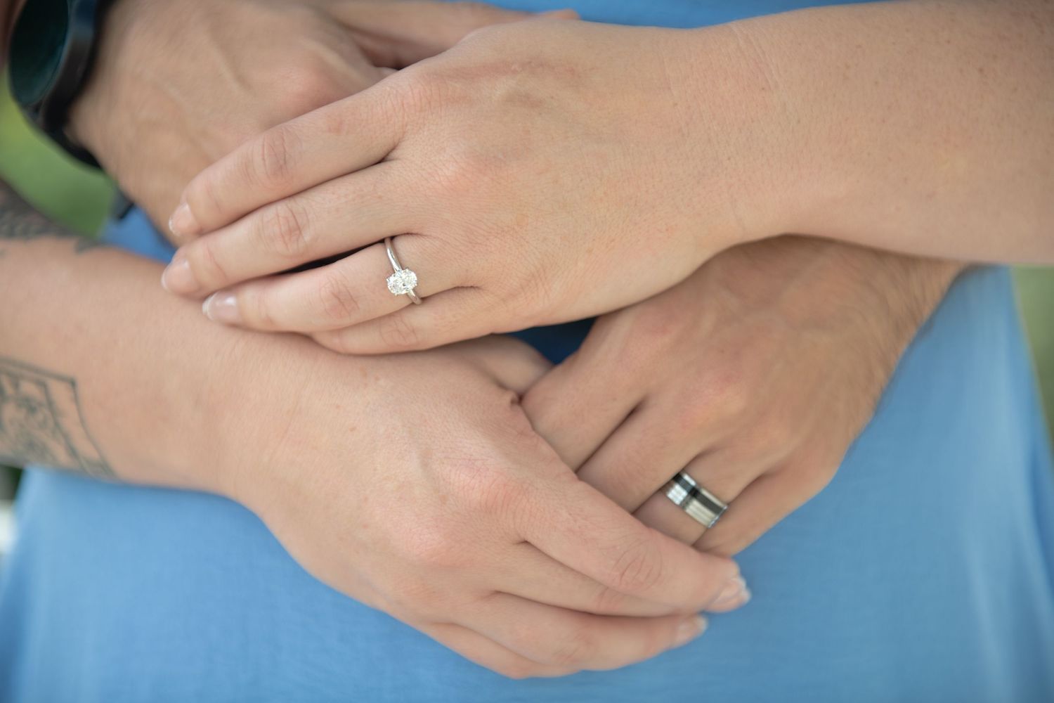Detail shot of hands displaying a new engagement ring against a blue background.
