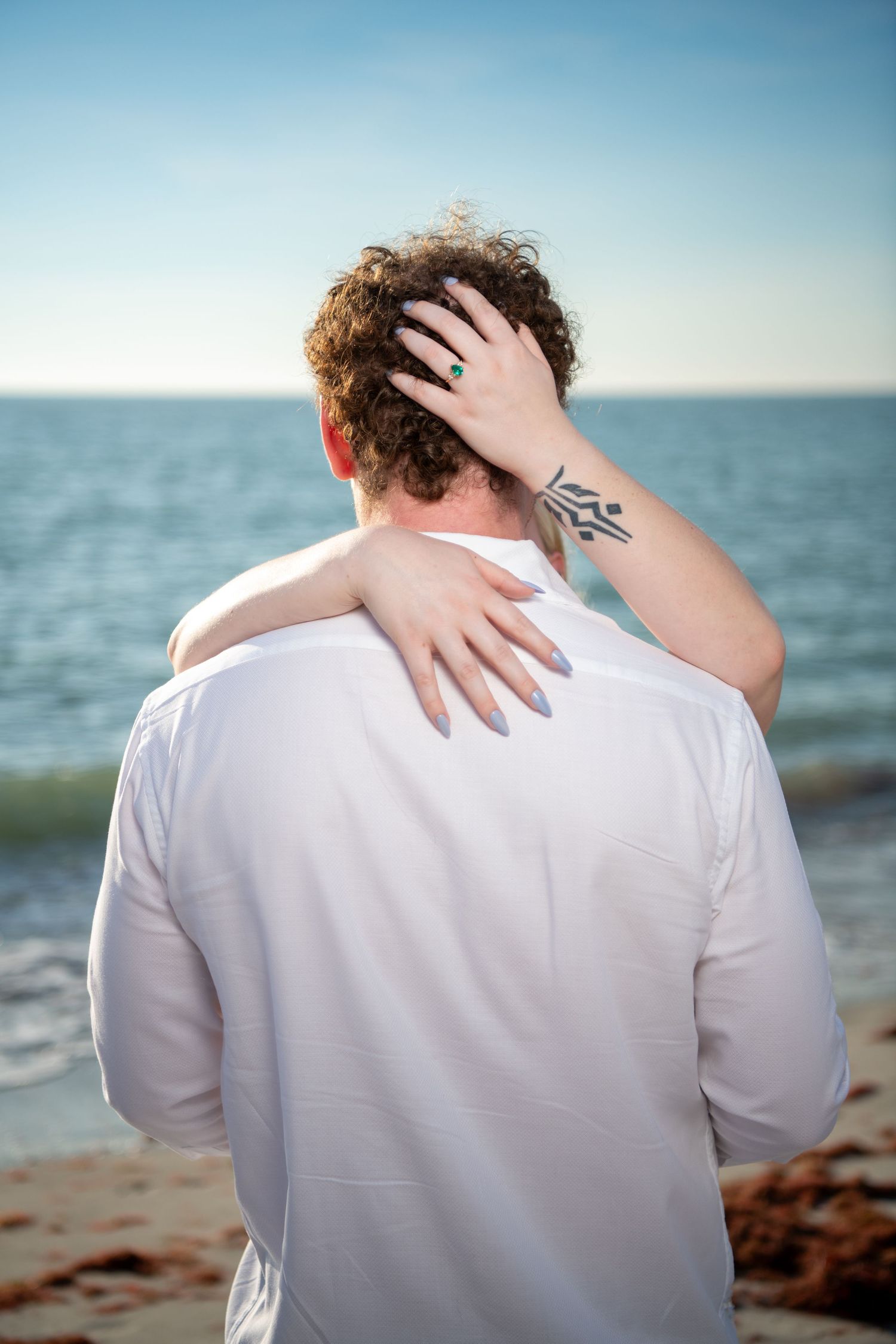 Back view portraits showing intimate embraces on a sunny beach. Engagement photoshoot. Couples photos.
