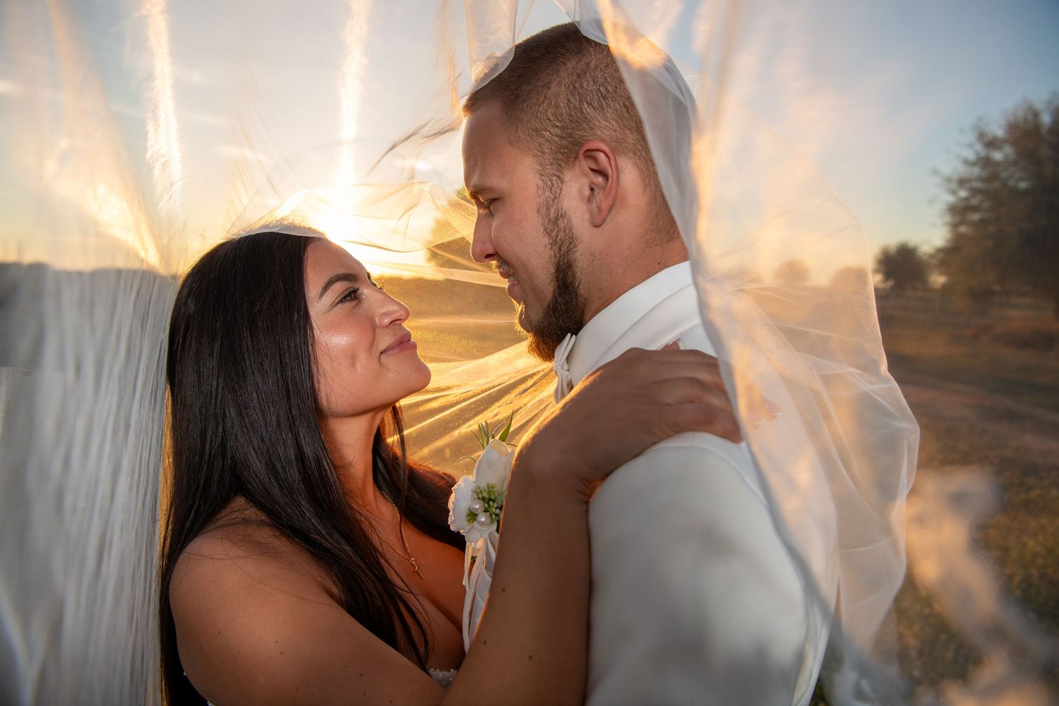 A loving couple embraces during their sunset wedding photoshoot with dramatic veil effects. Wedding photography.