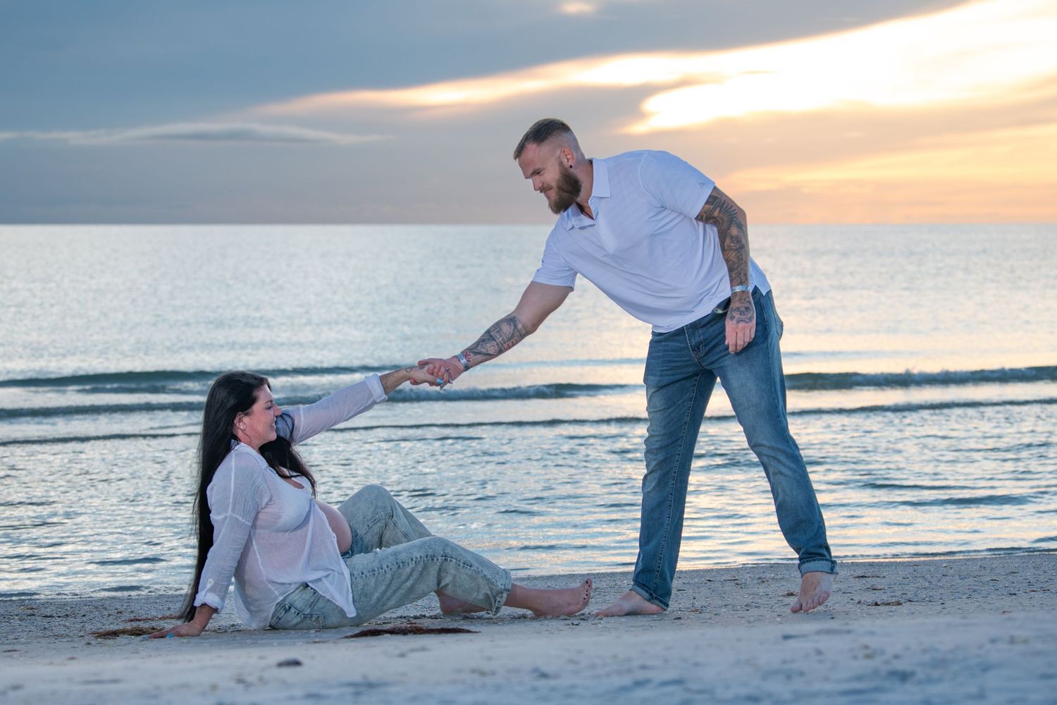 Playful couple poses on beach during sunset photoshoot. Maternity photoshoot.