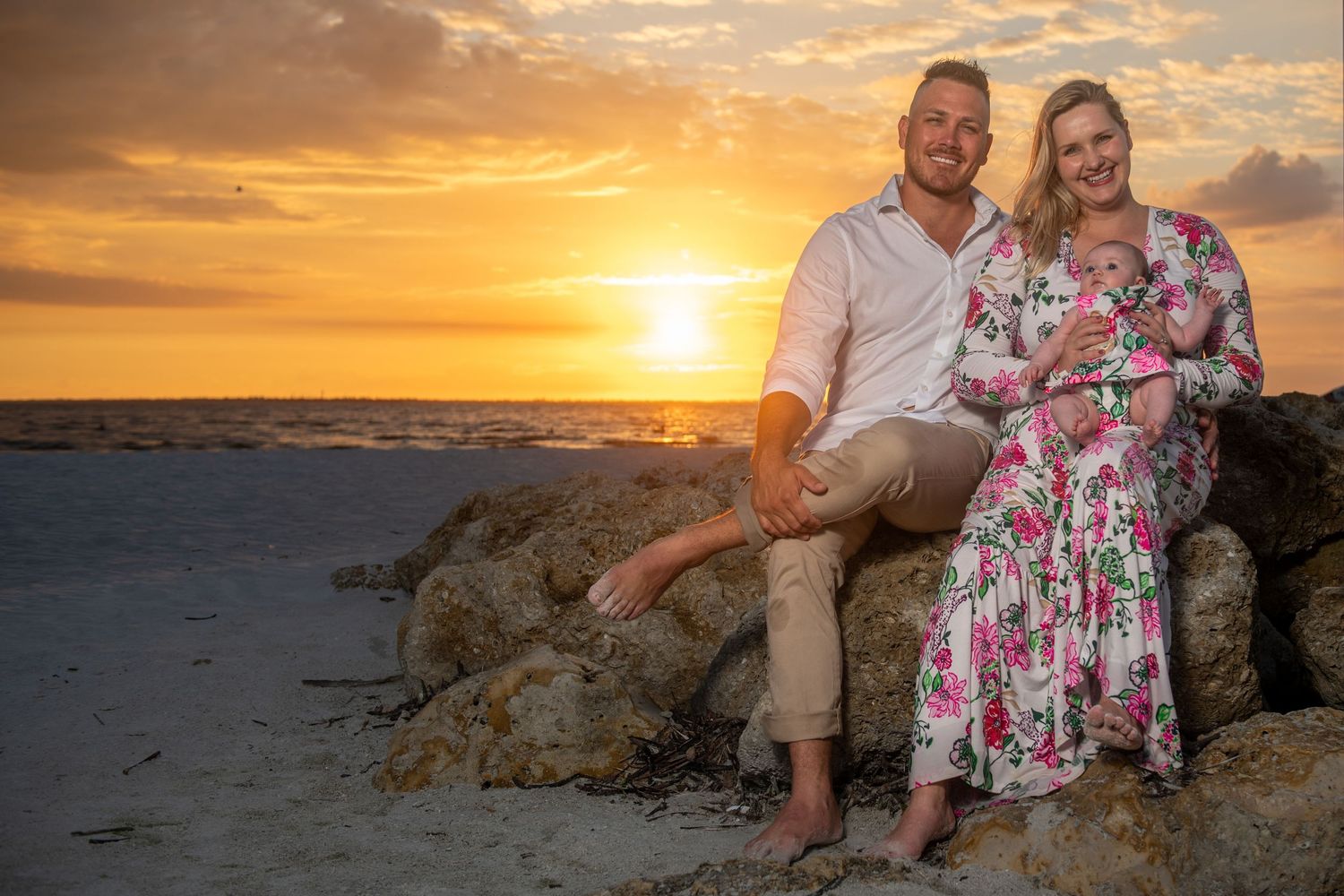 A sunset beach portrait session featuring a couple posing on coastal rocks with orange sky backdrop.