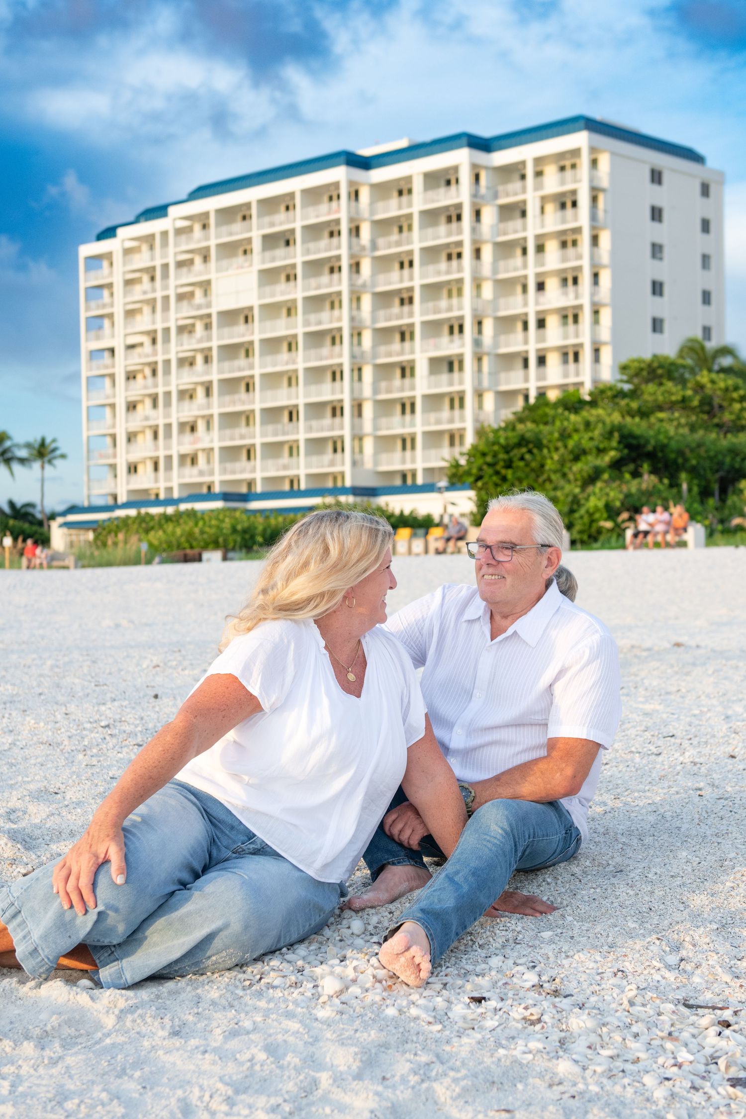 Couple relaxing on beach with beachfront condo building in background.