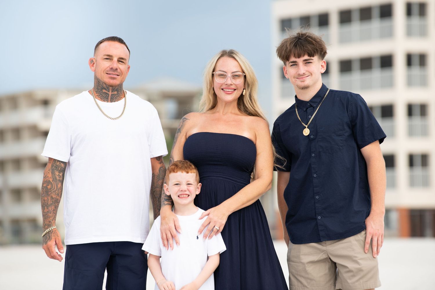 Family group photo session on bright sunny beach with coastal buildings.