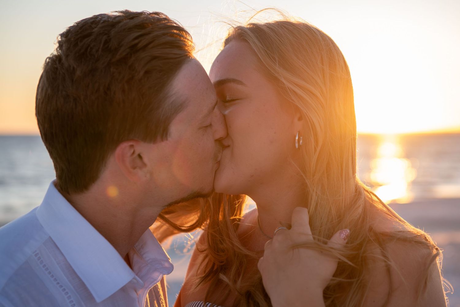 Romantic couple sharing an intimate moment at sunset on the beach with golden light in the background.