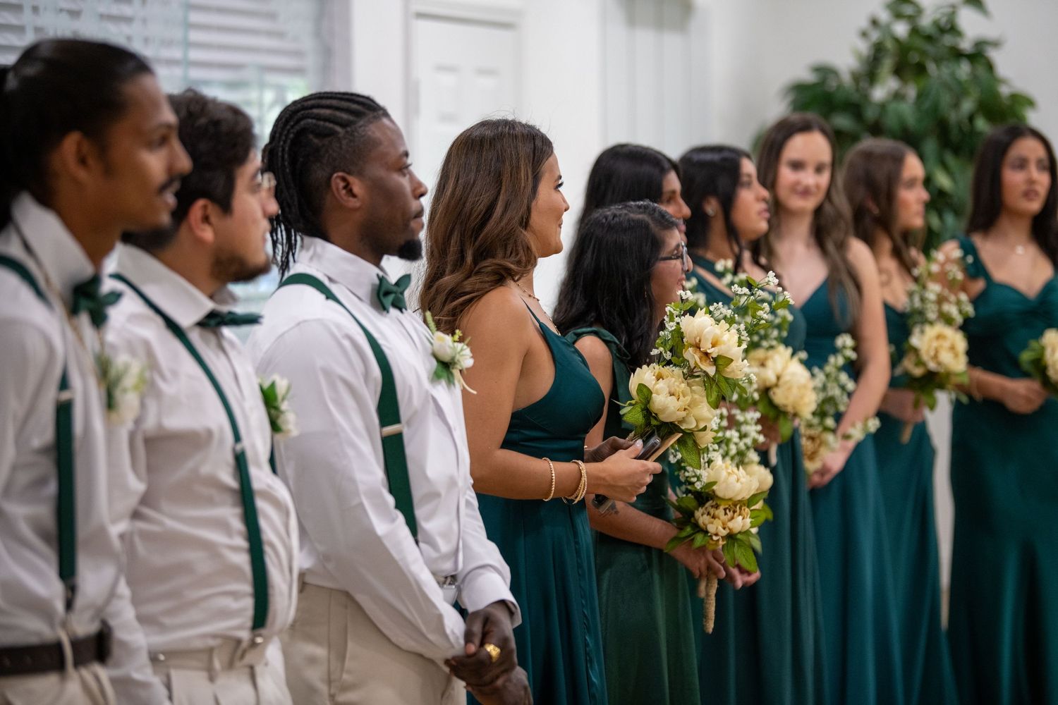 Wedding party in emerald green dresses and white attire standing together during ceremony. Wedding photography.