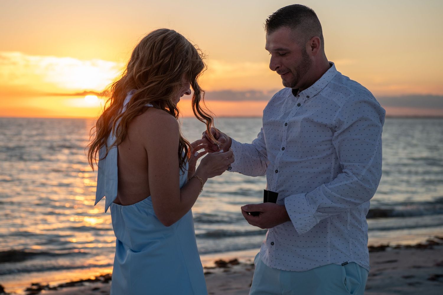 Couple embraces on beach at sunset with ocean waves in background. Engagement photoshoot. Couples photos.
