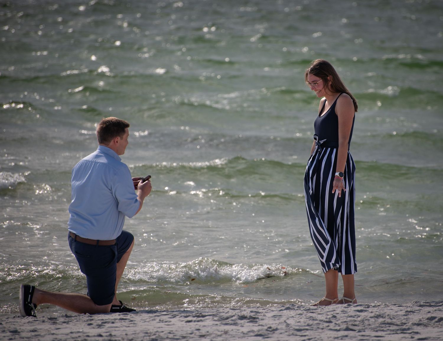 A beach proposal scene with waves crashing in the background.