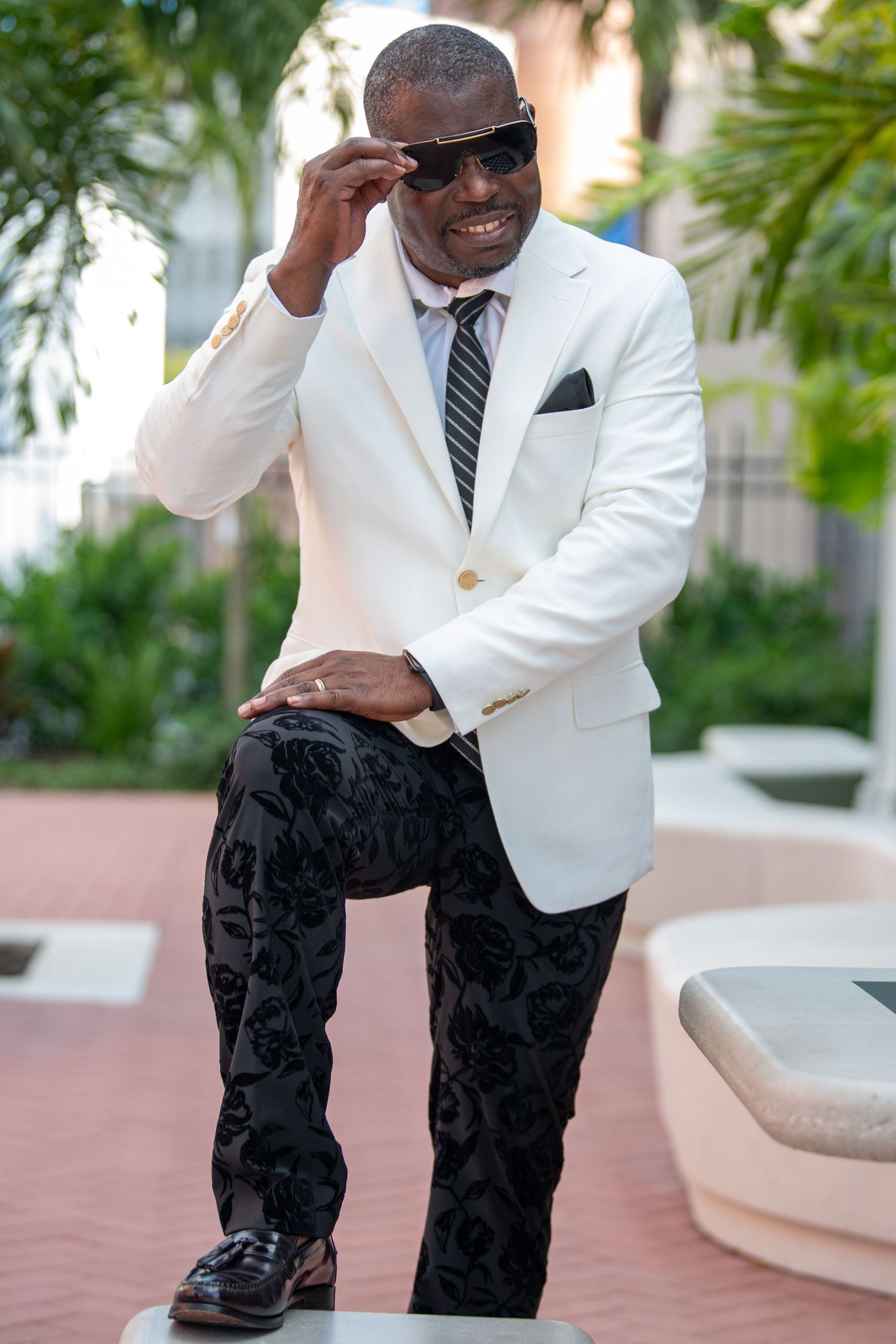 Casual outdoor portrait of a person in white blazer and patterned pants.