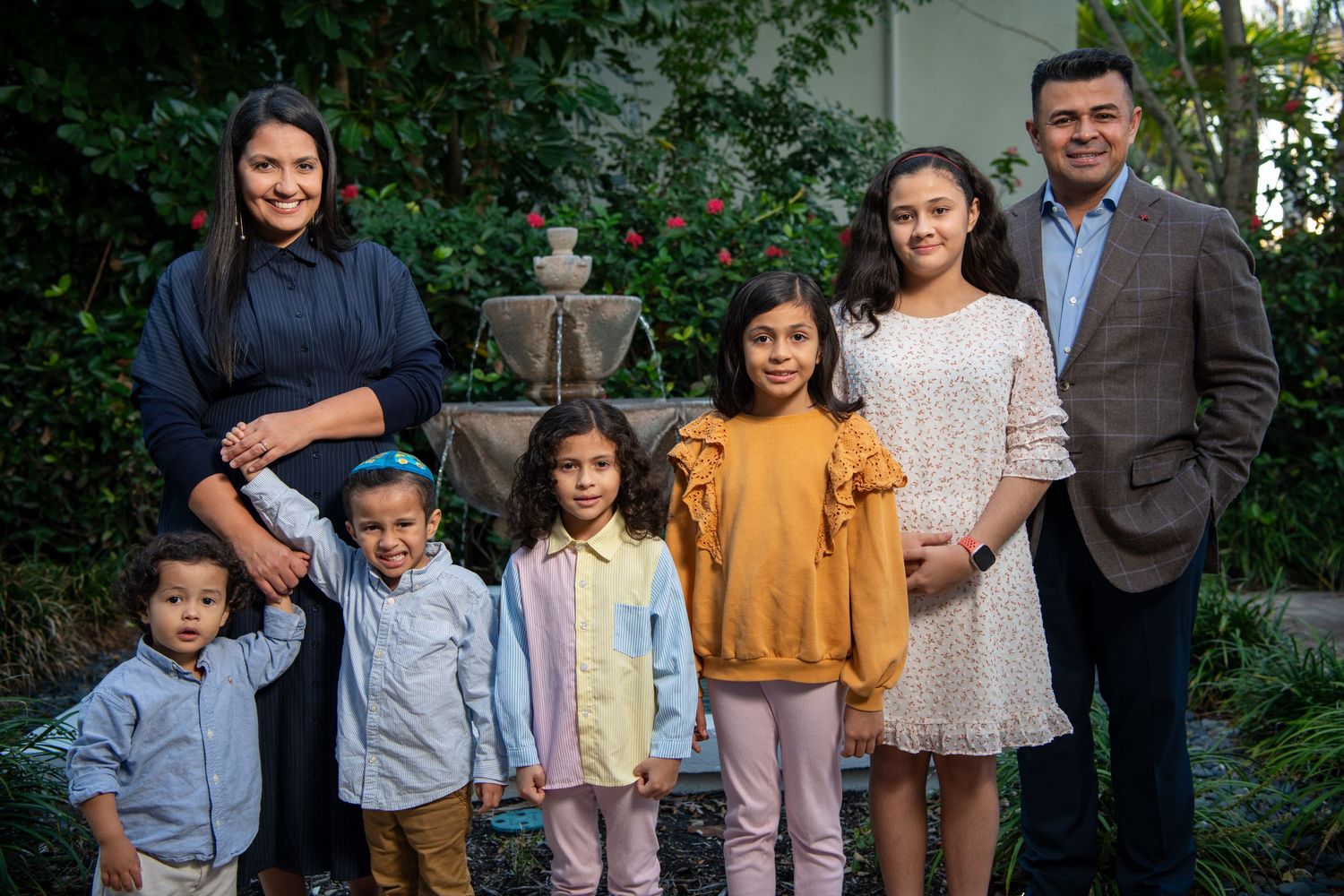 A family poses together outdoors near a garden fountain during golden hour. Family photoshoot.