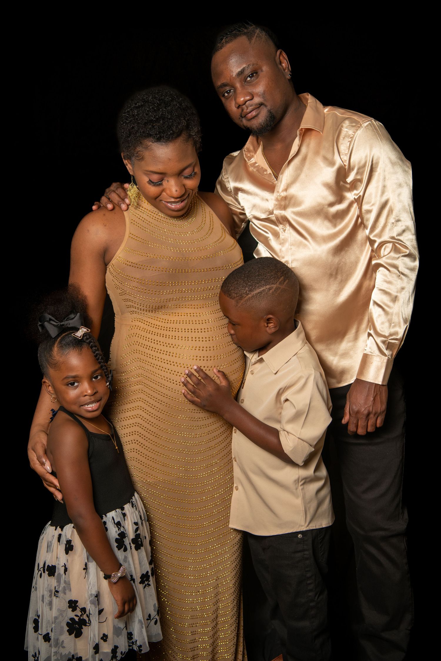 Family maternity portrait with children in formal attire against dark backdrop. Maternity photoshoot.