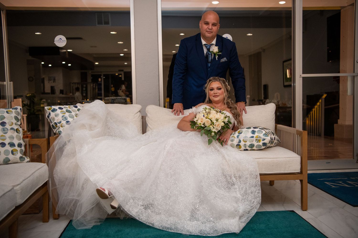 A bride in a flowing white gown sits in a modern indoor venue.