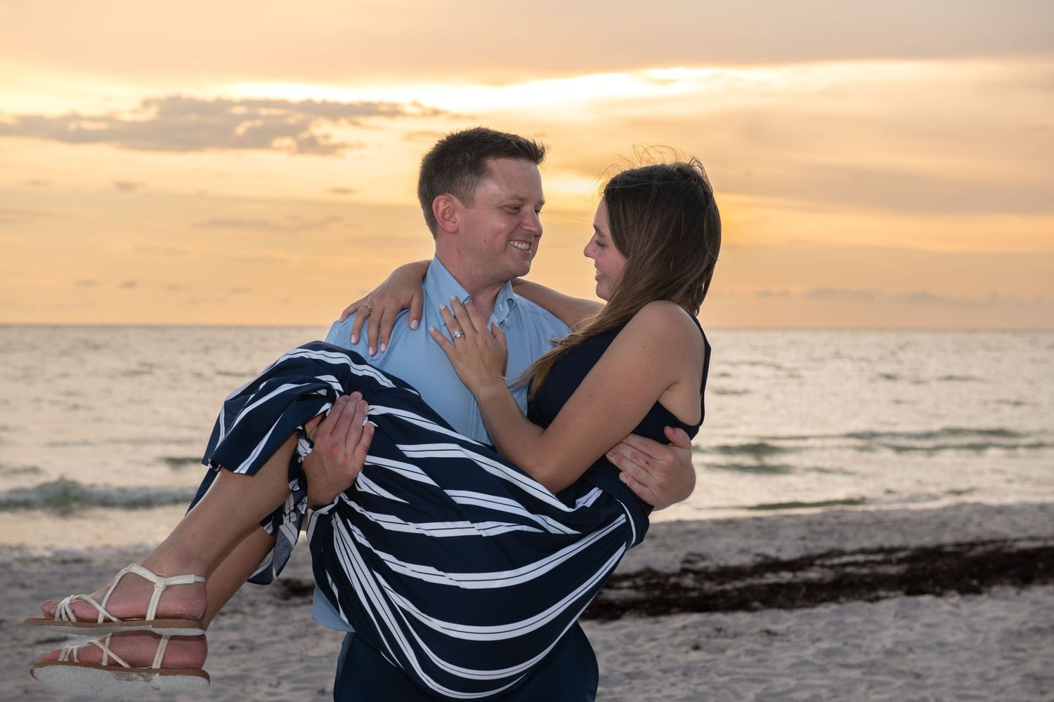 A romantic beach photoshoot featuring a couple in coordinated outfits dancing by the ocean at sunset.