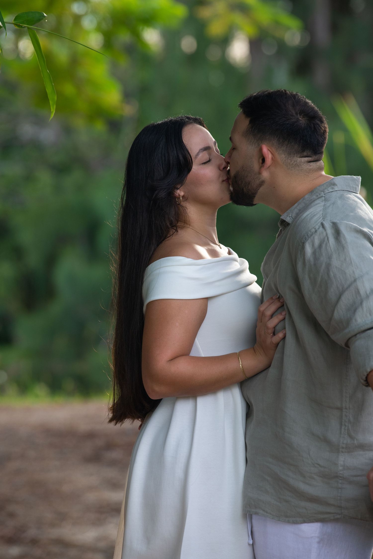 A couple in white and gray attire share romantic moments in a lush garden setting.