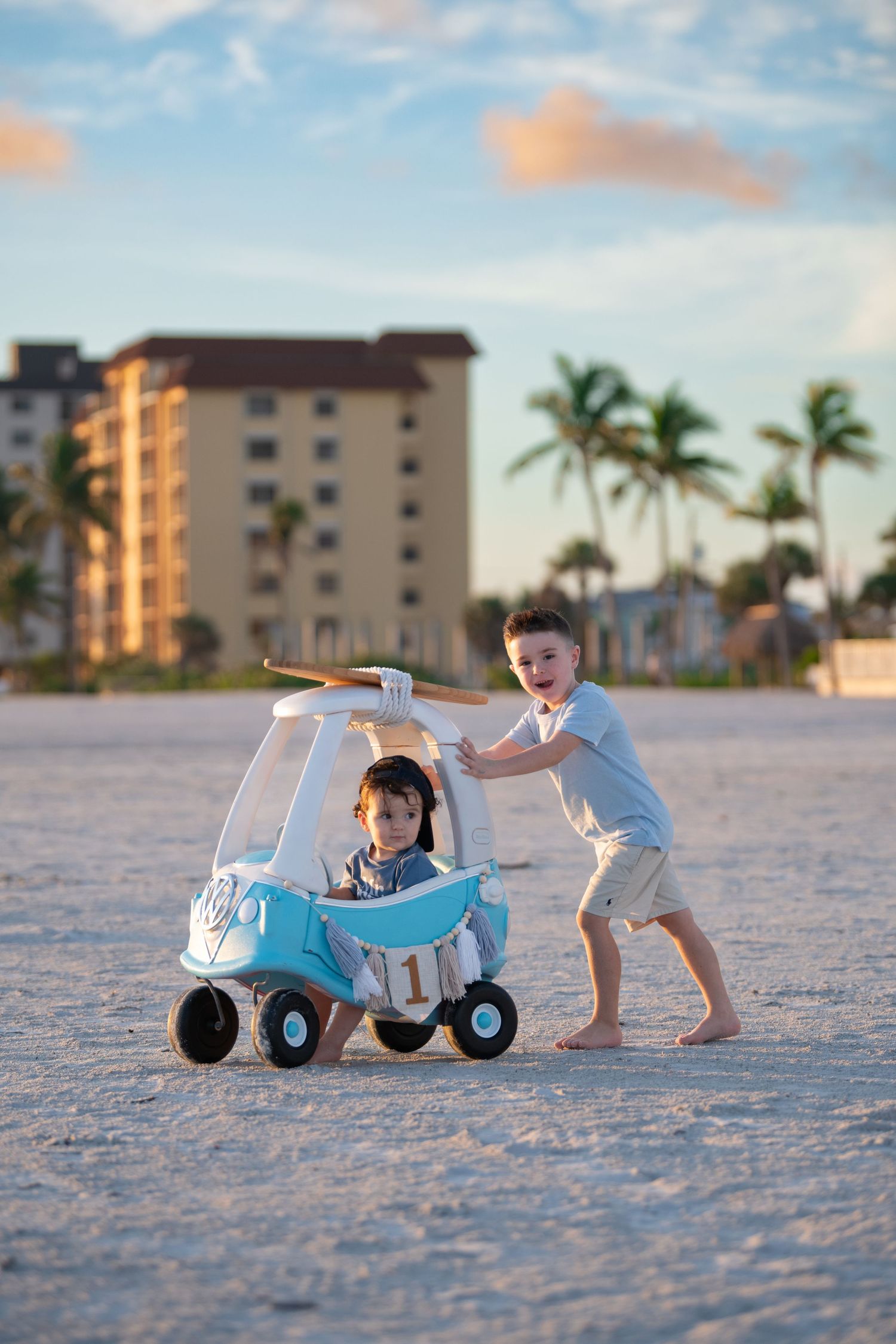 Children playing with blue toy car on sandy beach at sunset.