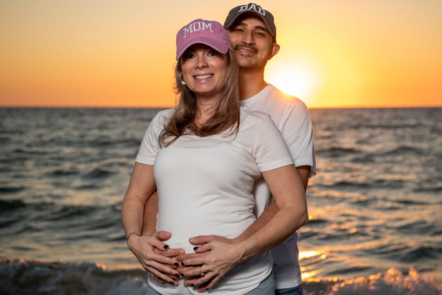 A romantic maternity photo of a couple embracing on the beach at sunset with the ocean in the background. Maternity photoshoot. Couples phot