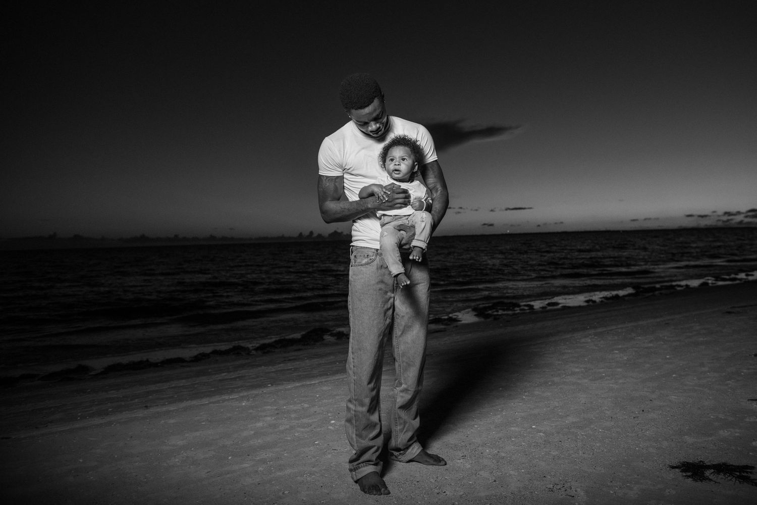 Black and white portrait of people embracing on a beach at dusk.