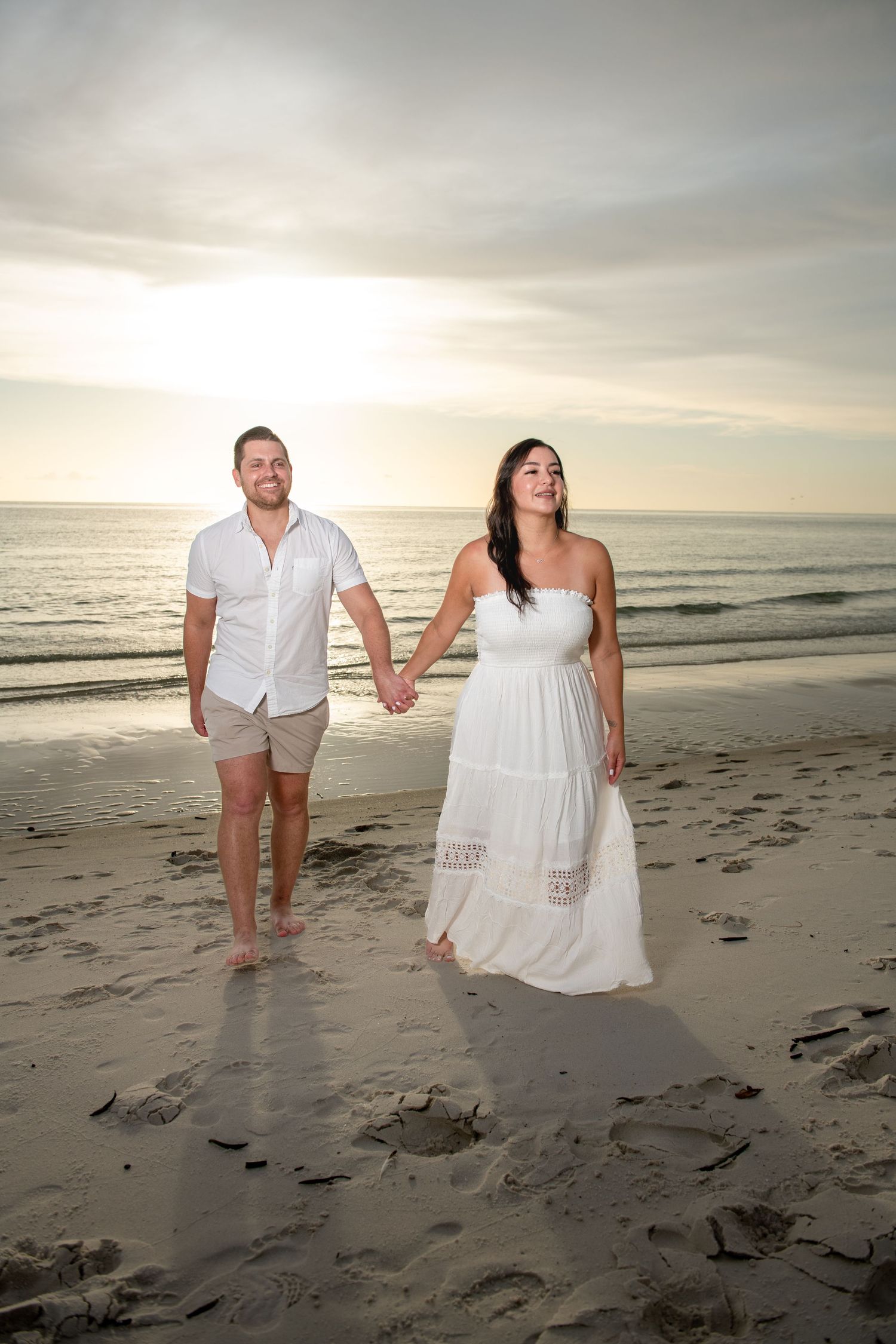 Playful beach photoshoot with couple walking in sand during sunset.