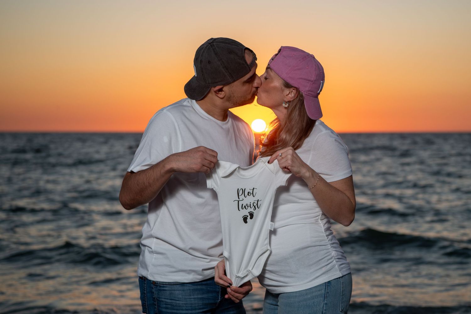 Couple holding baby announcement onesie during beach sunset photoshoot. Maternity photoshoot. Couples photos.