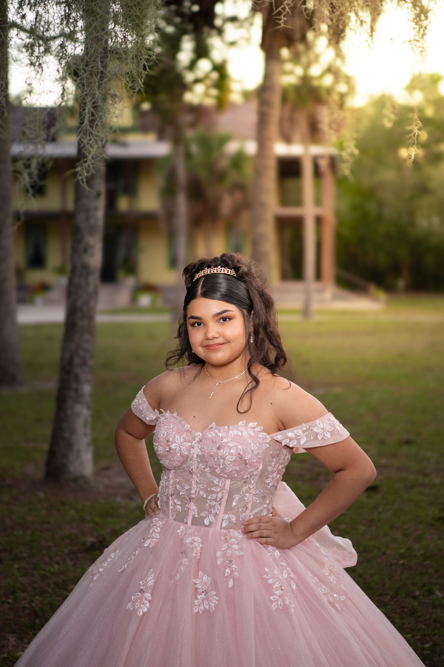 A person in a pink princess ball gown poses gracefully in an outdoor garden setting at sunset. Quinceañera photos.
