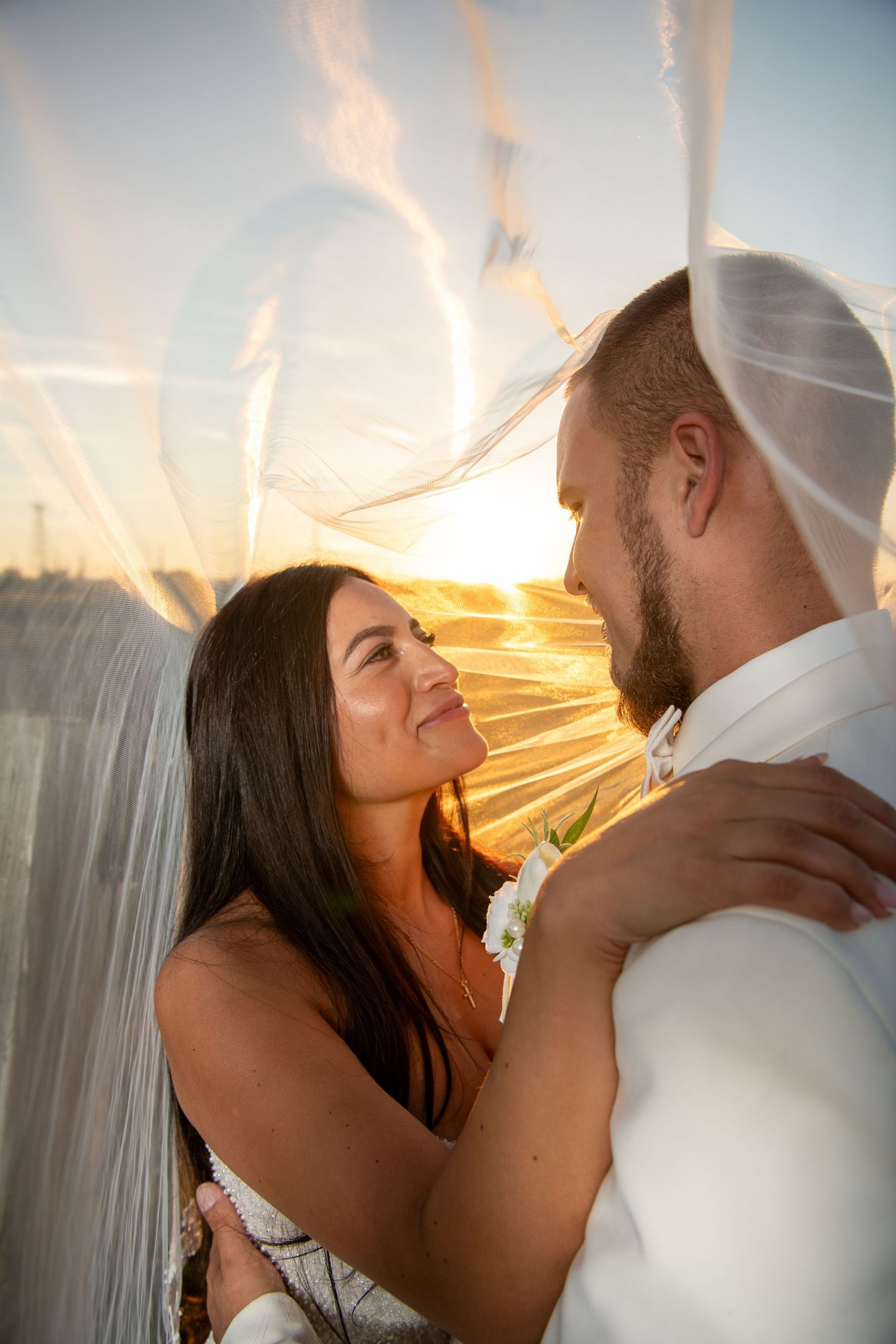 A romantic sunset portrait of newlyweds with the bride's veil catching golden light. Wedding photography.
