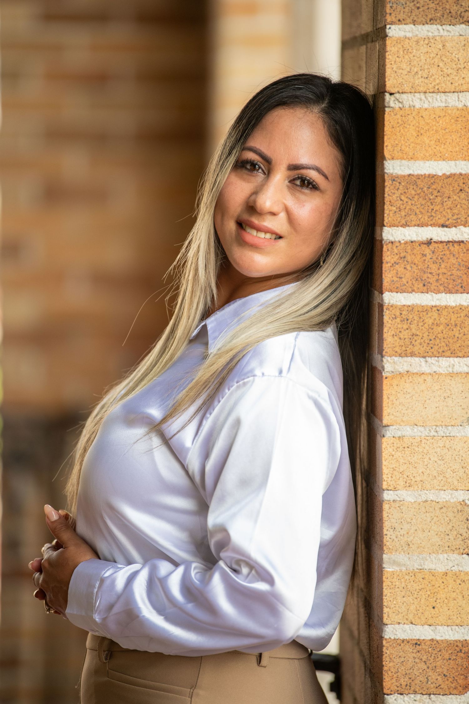 Professional headshot against brick wall showing warm, confident expression.