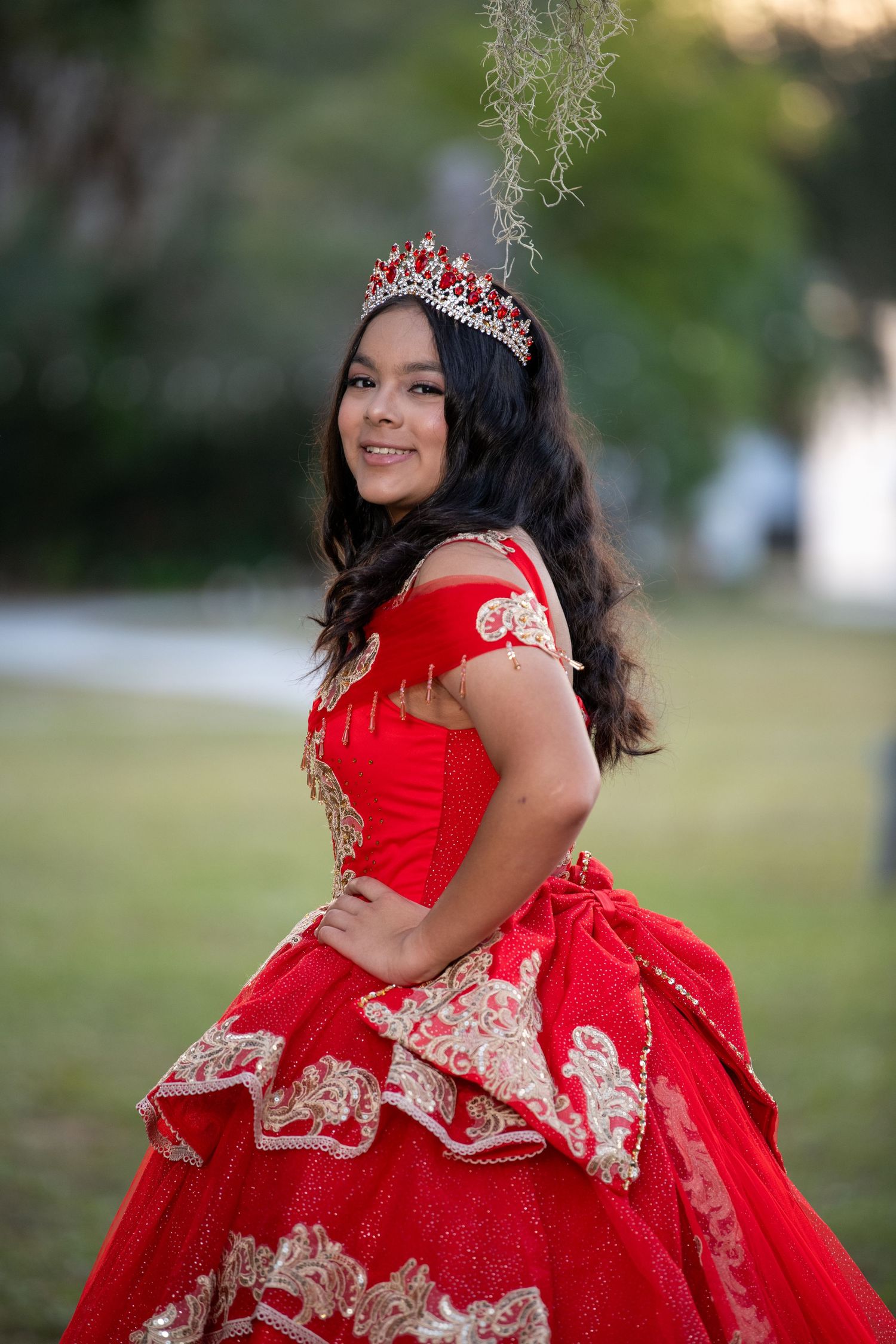 Quinceañera celebration featuring ornate red and gold ball gown in outdoor setting. Quinceañera photoshoot.