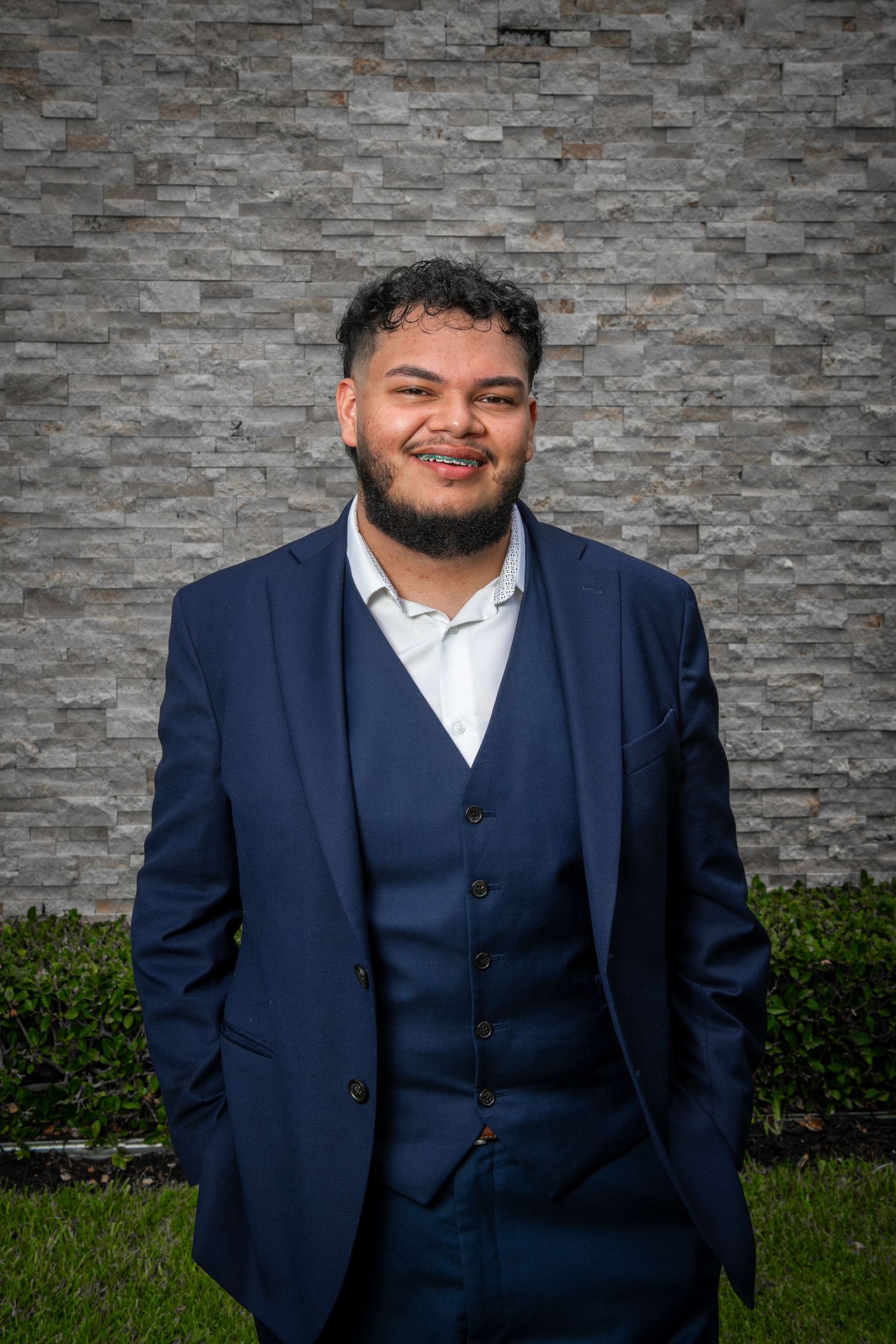 Professional headshot in navy suit against textured stone wall background.