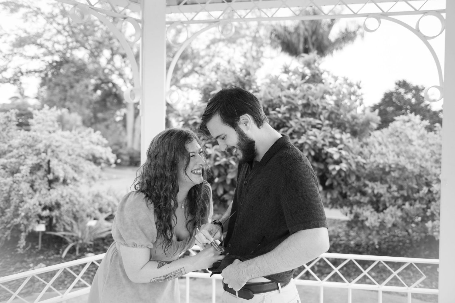 Romantic moment captured in black and white under an ornate white gazebo.