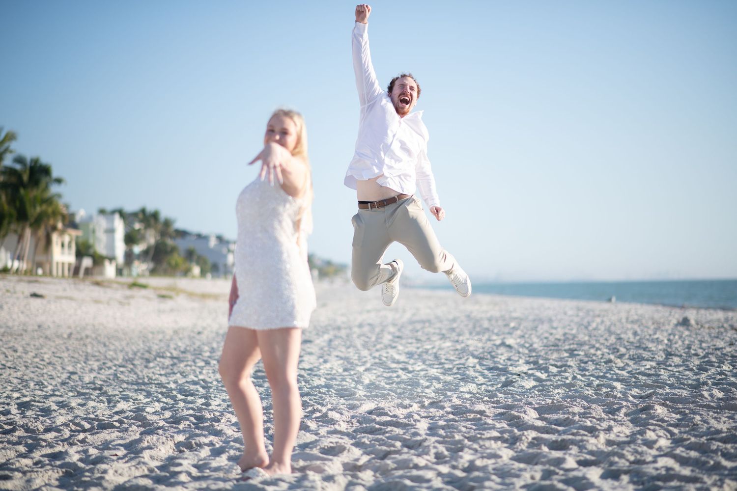 Joyful couple jumping and celebrating on a sunny white sand beach. Engagement photoshoot. Couples photos.