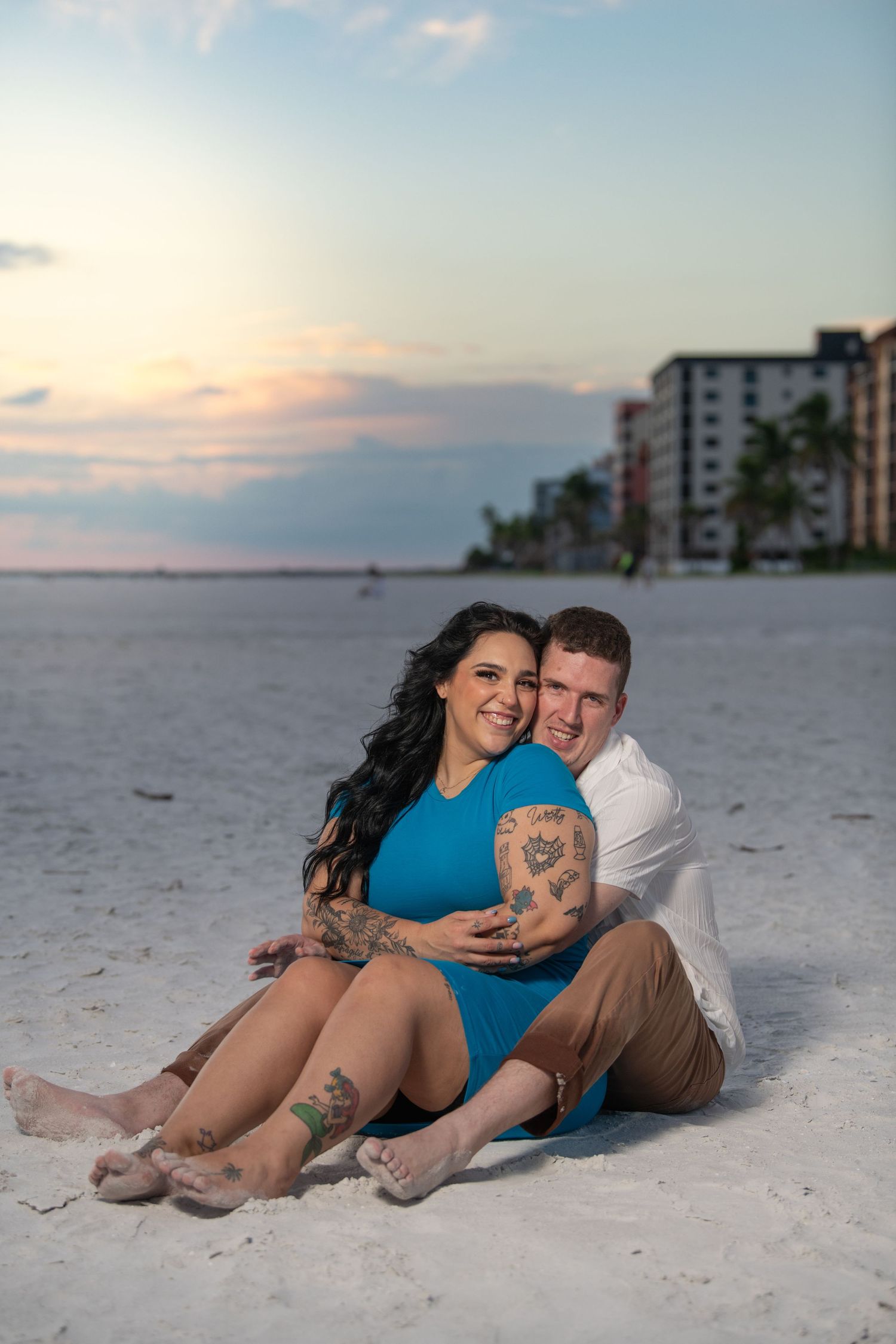 A couple in casual attire shares an intimate moment on the beach at sunset.