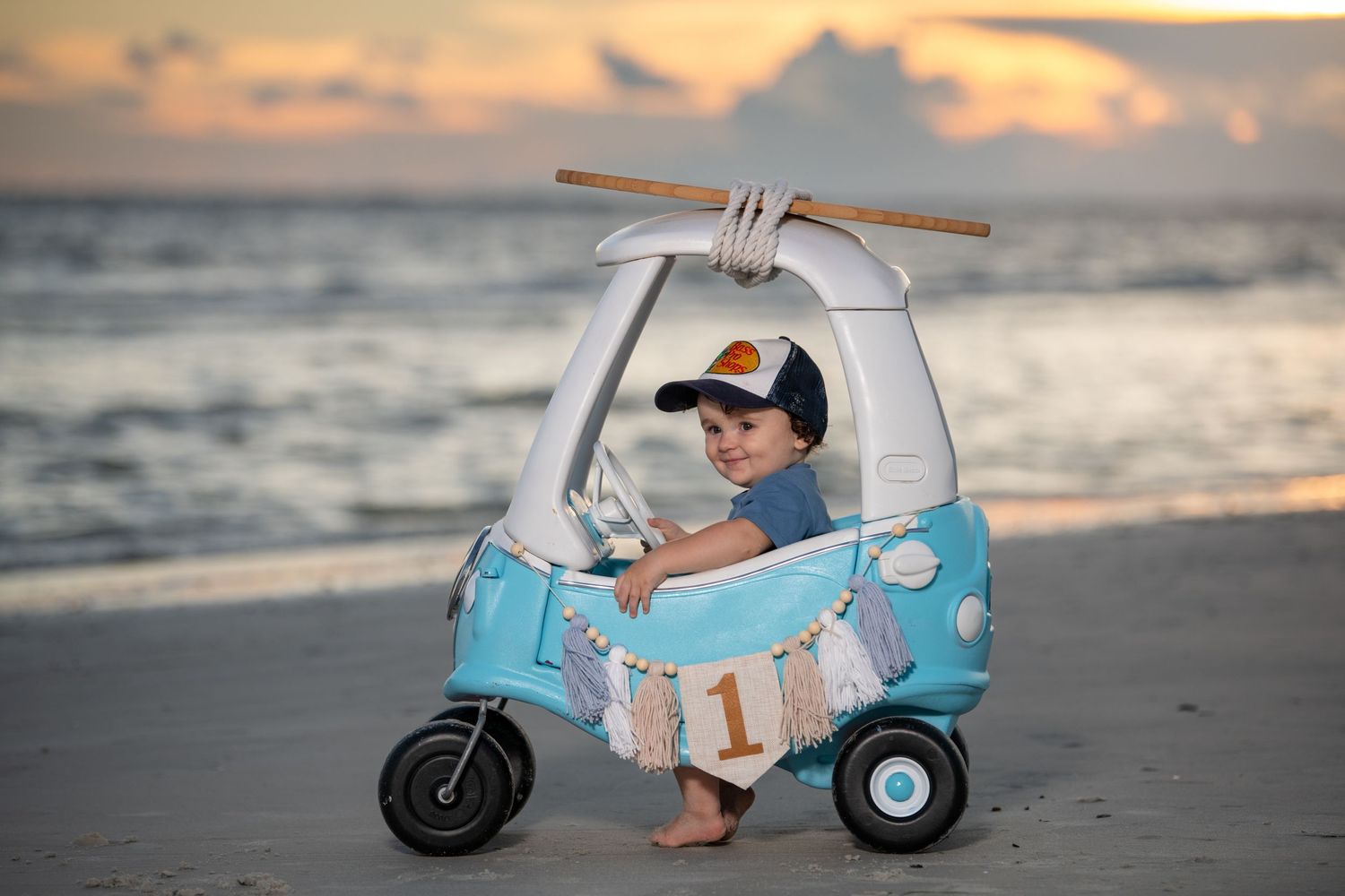 Child sitting in vintage-style toy scooter on beach during golden hour.