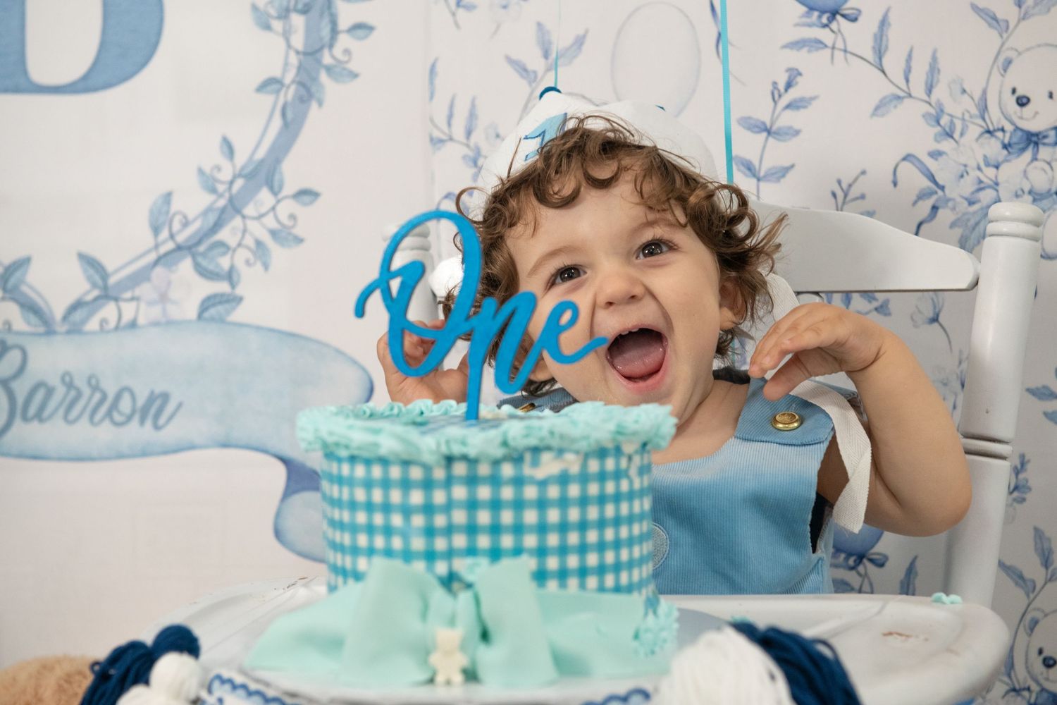 A first birthday celebration setup with a blue and white gingham cake and decorative banner.