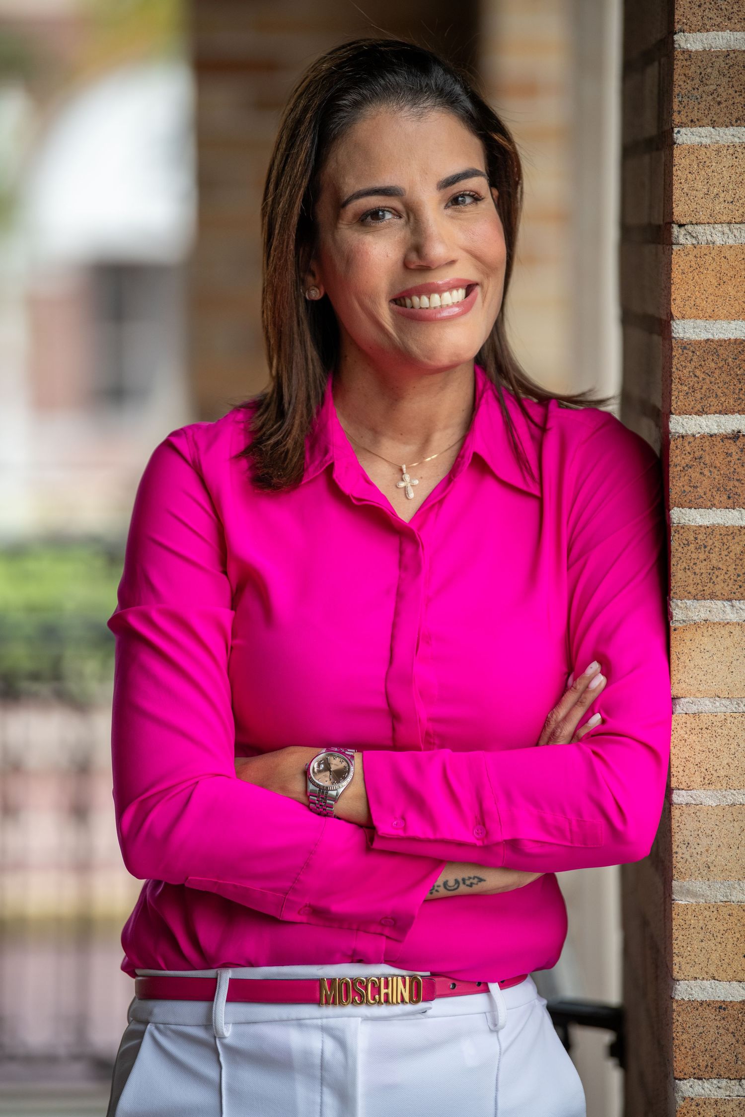 Executive style portrait featuring bright pink button-down shirt and white pants against brick wall.
