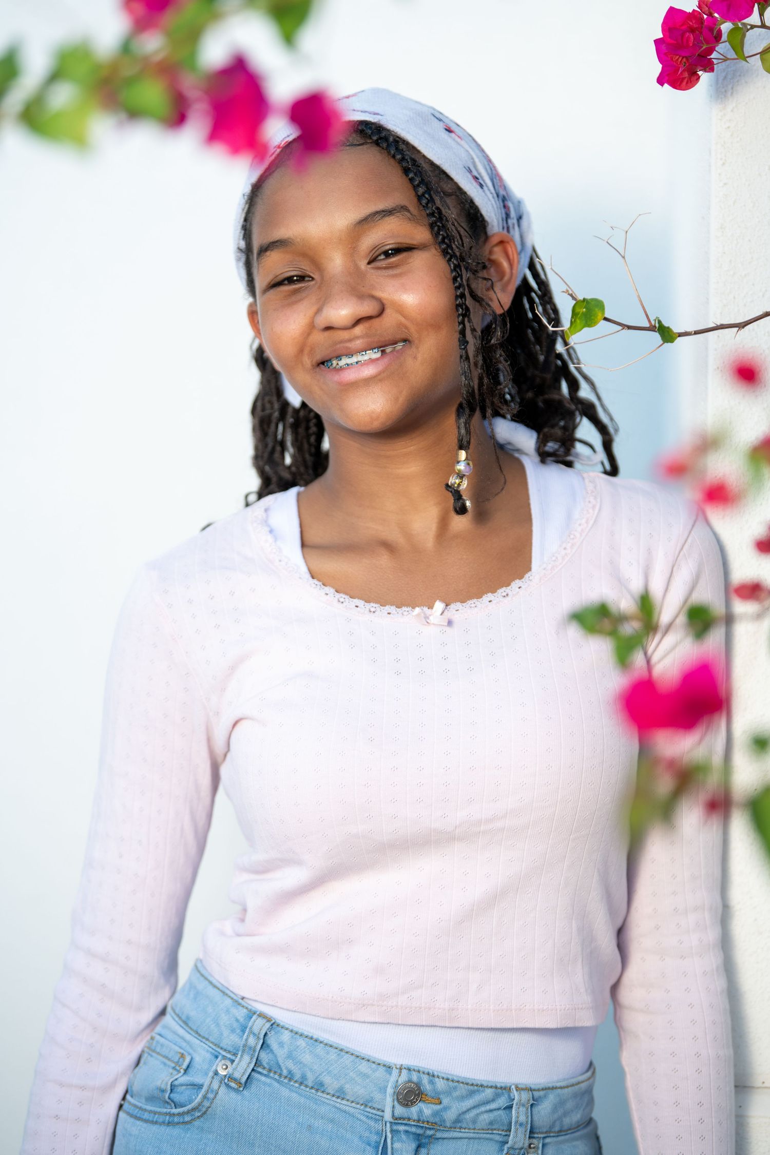 Cheerful portrait with dangling earrings against white wall and pink flowers. Headshots.