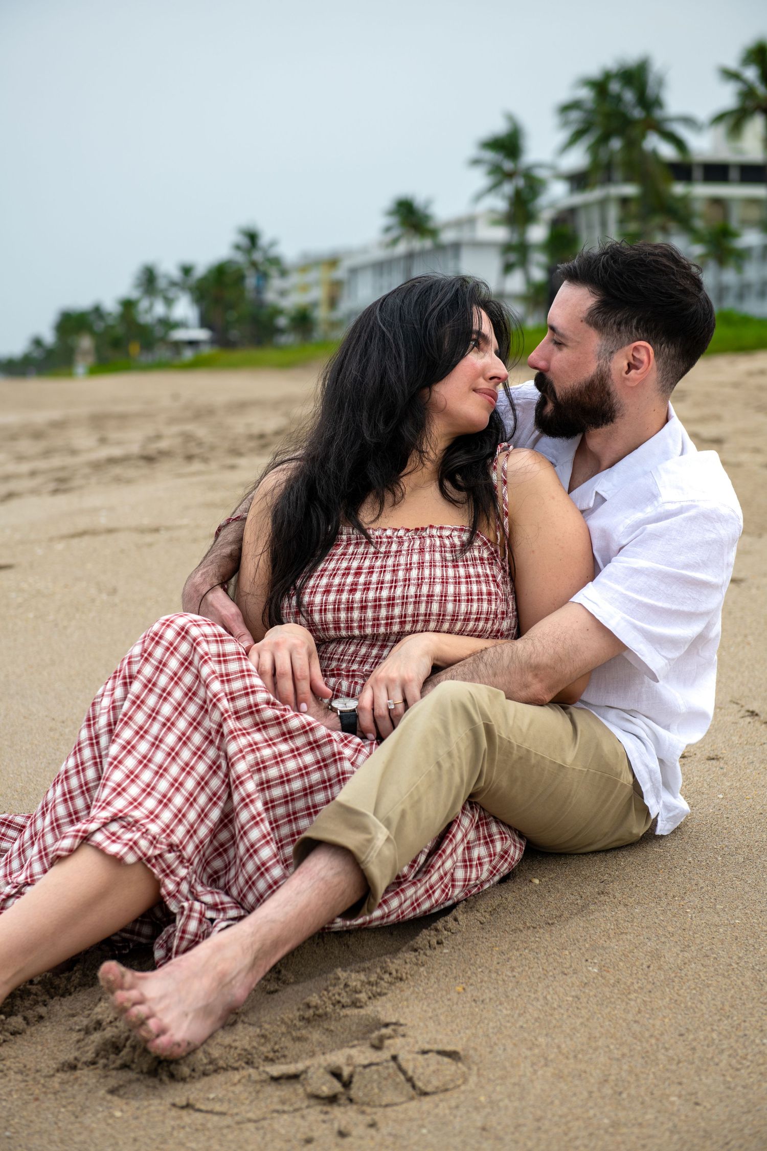 A couple lounges romantically on a tropical beach with palm trees in the background.