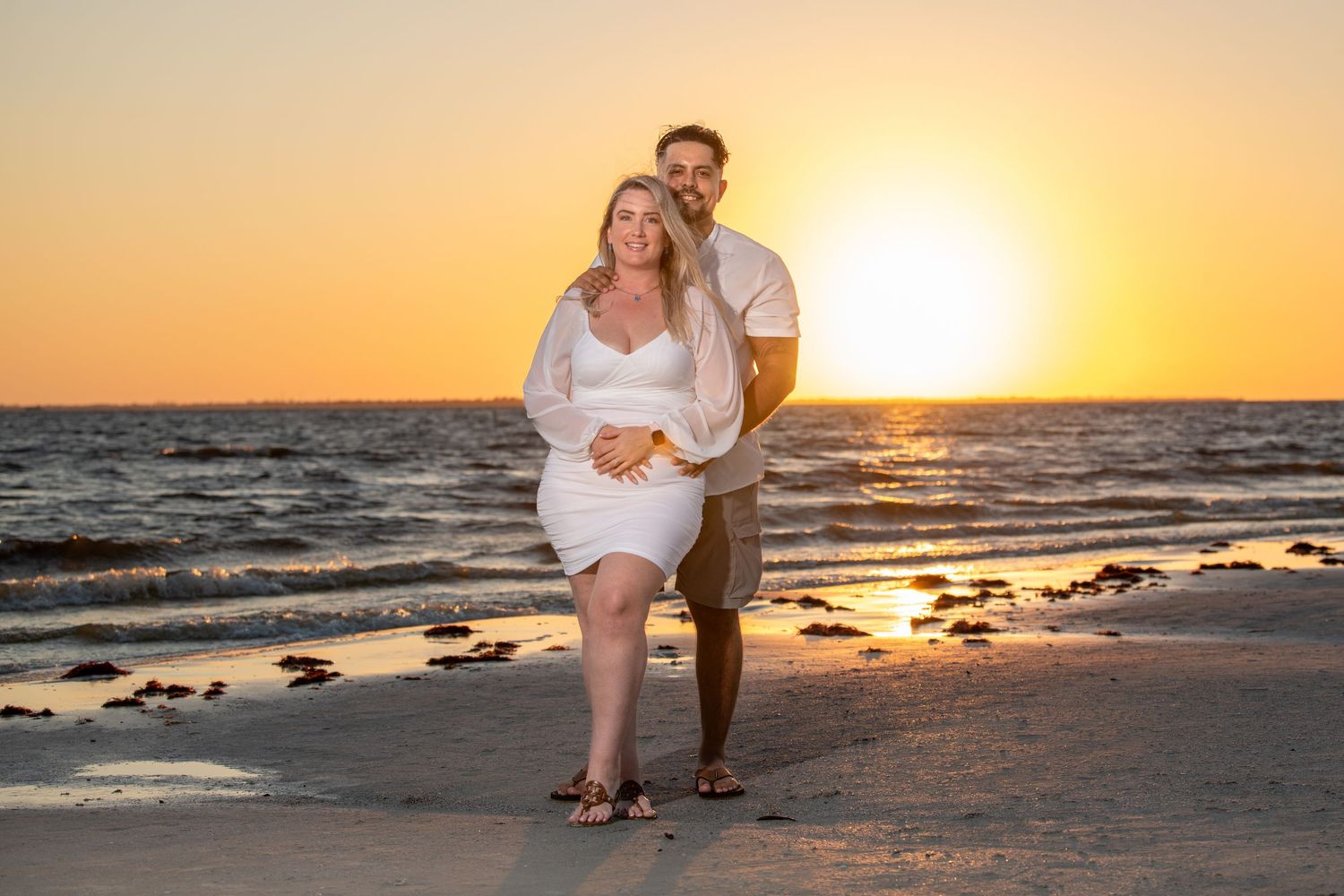 Beach engagement session with couple posing against dramatic sunset sky.