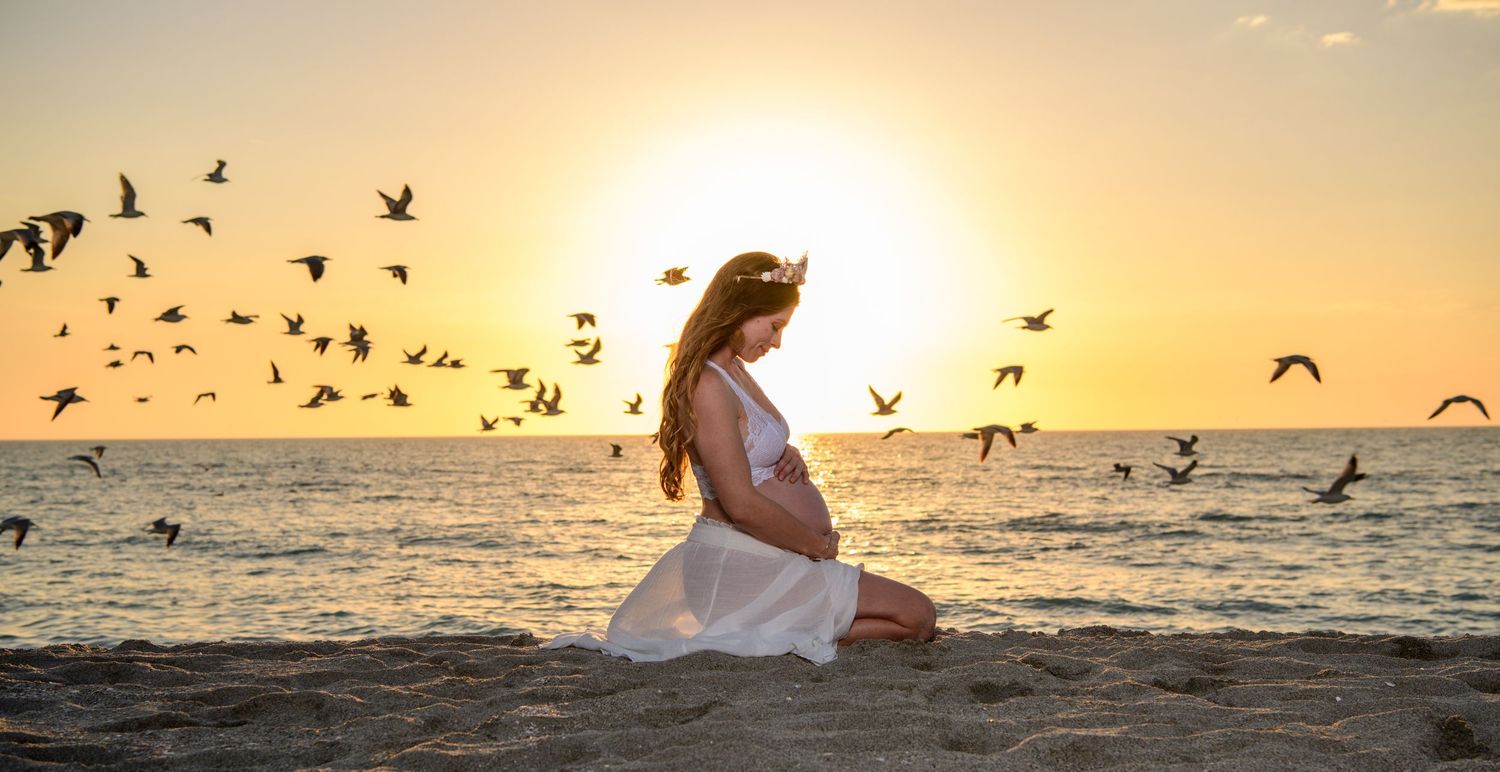 Romantic beach photoshoot at sunset with seabirds flying overhead against an orange sky. Maternity photoshoot,