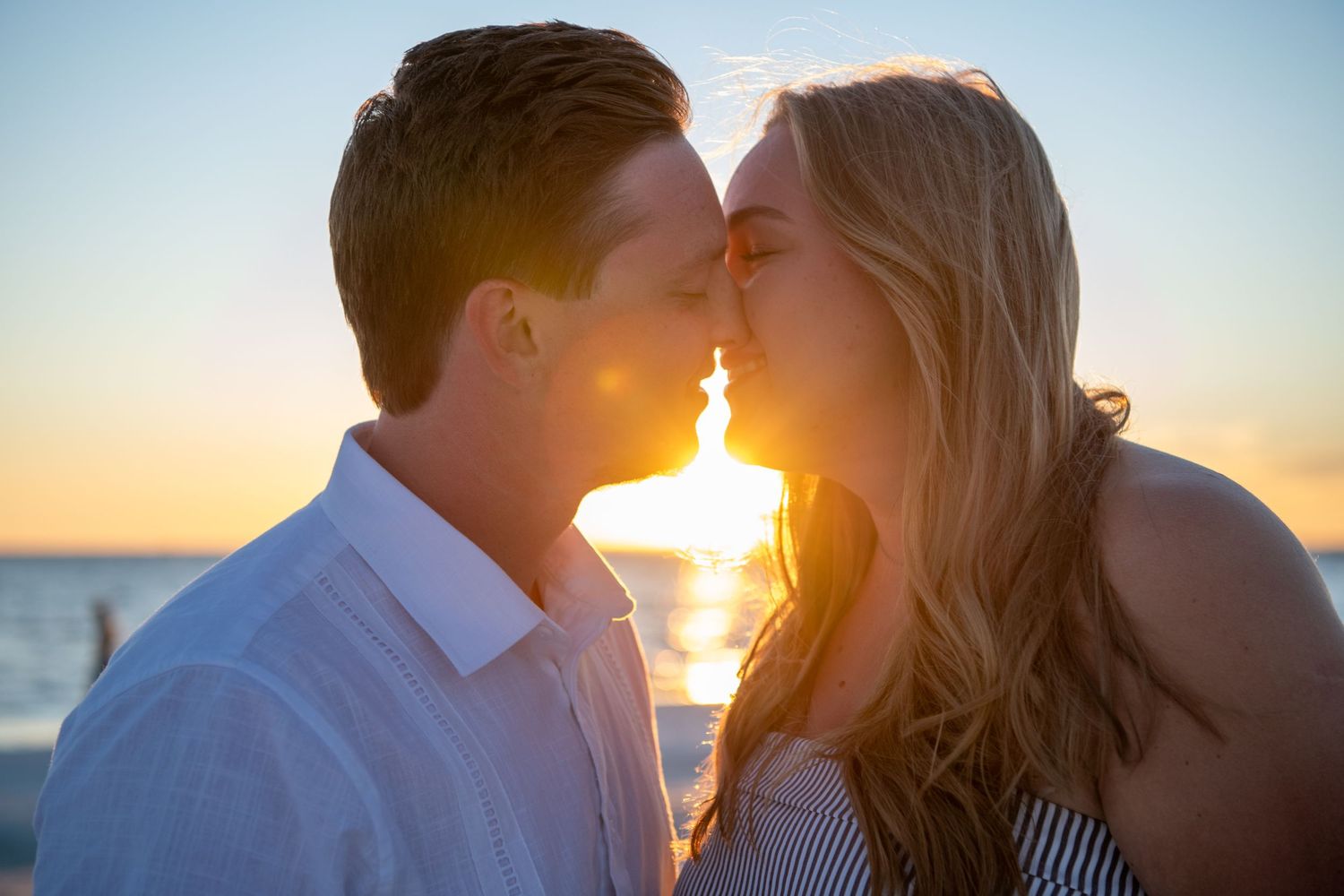 Tender moment between couple during beach sunset photoshoot with ocean waves behind them.
