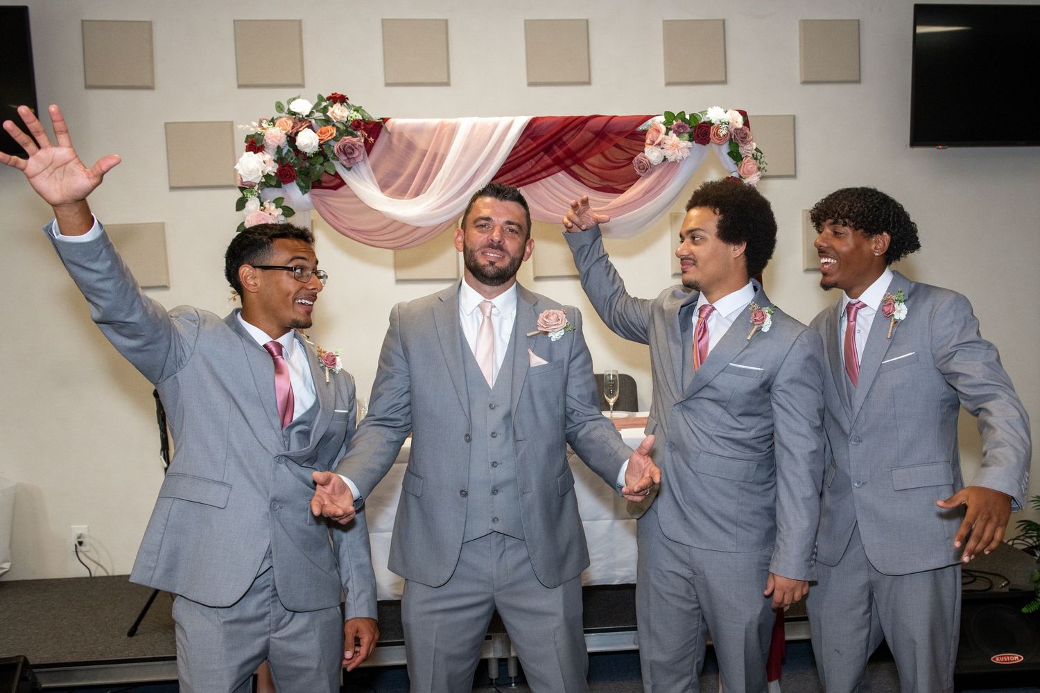 Groomsmen in gray suits pose playfully for a group photo at a wedding.