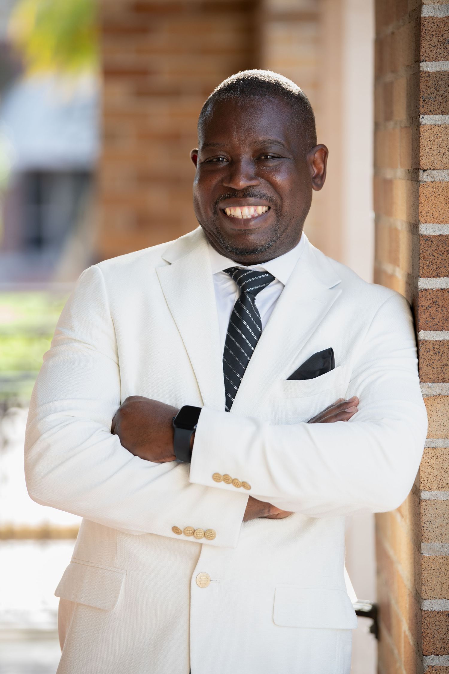 Professional wearing a white suit jacket and striped tie poses with crossed arms.