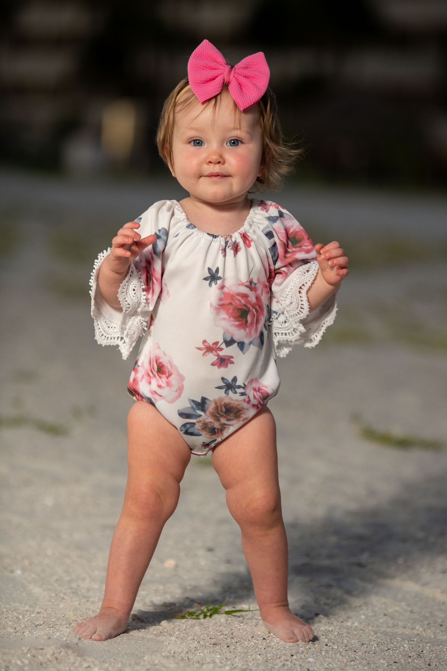 Floral romper and pink bow photographed on sandy ground.