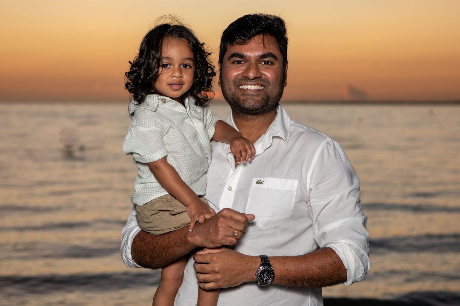 A family enjoys a sunset photoshoot at the beach with warm golden light reflecting off the ocean. Beach photoshoot. Family photoshoot,